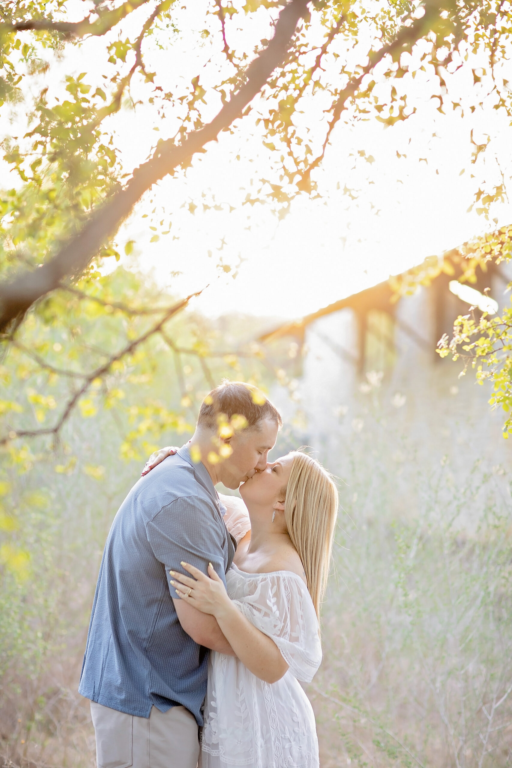 Couple walking hand-in-hand through the trails of Government Canyon State Natural Area during a golden hour engagement session with warm sunlight, natural Hill Country scenery, and candid romantic moments before their August wedding at The Gardens at Old Town Helotes.