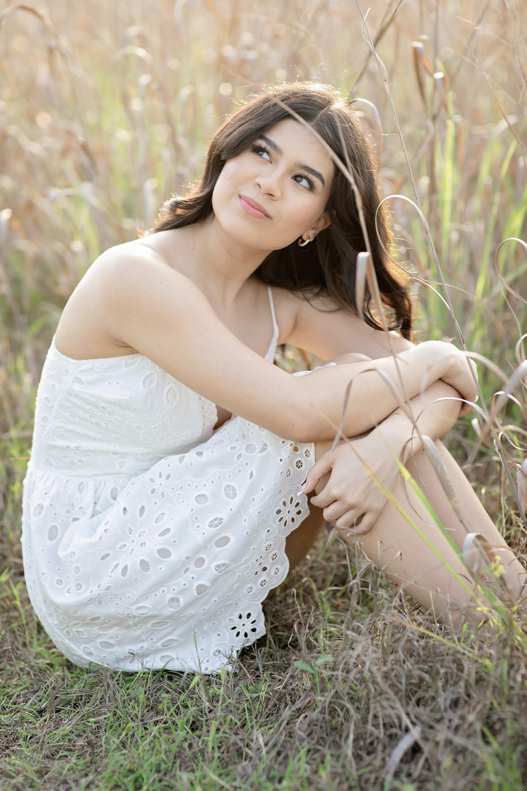 High school senior standing barefoot in the river at Cibolo Nature Center & Farm during golden hour, wearing a flowing white dress surrounded by natural Texas Hill Country scenery, garden landscapes, and tall glowing fields for a relaxed outdoor senior session.