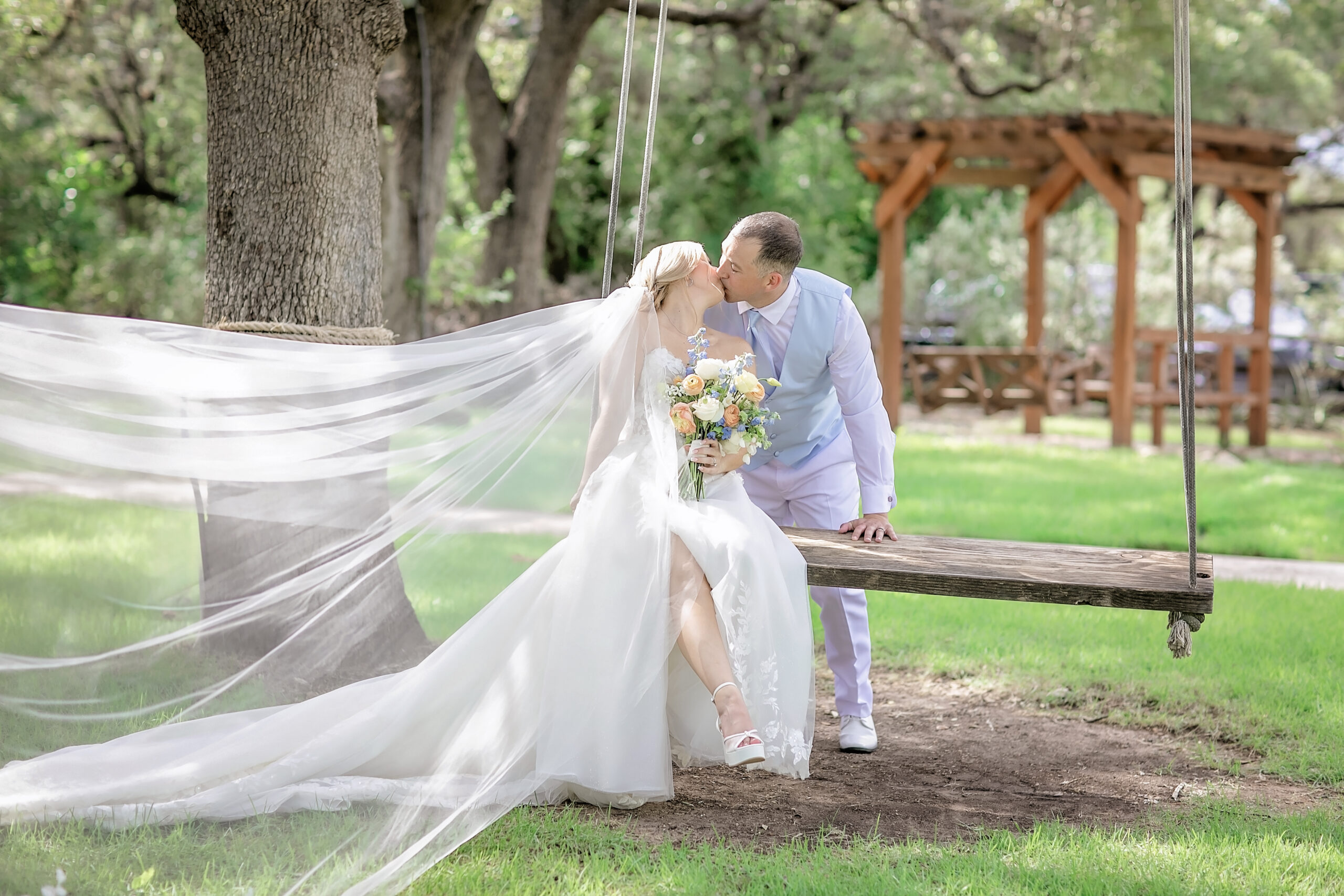Courtnie and Taylor share a romantic kiss on a swing during their summer wedding at Gardens at Old Town Helotes