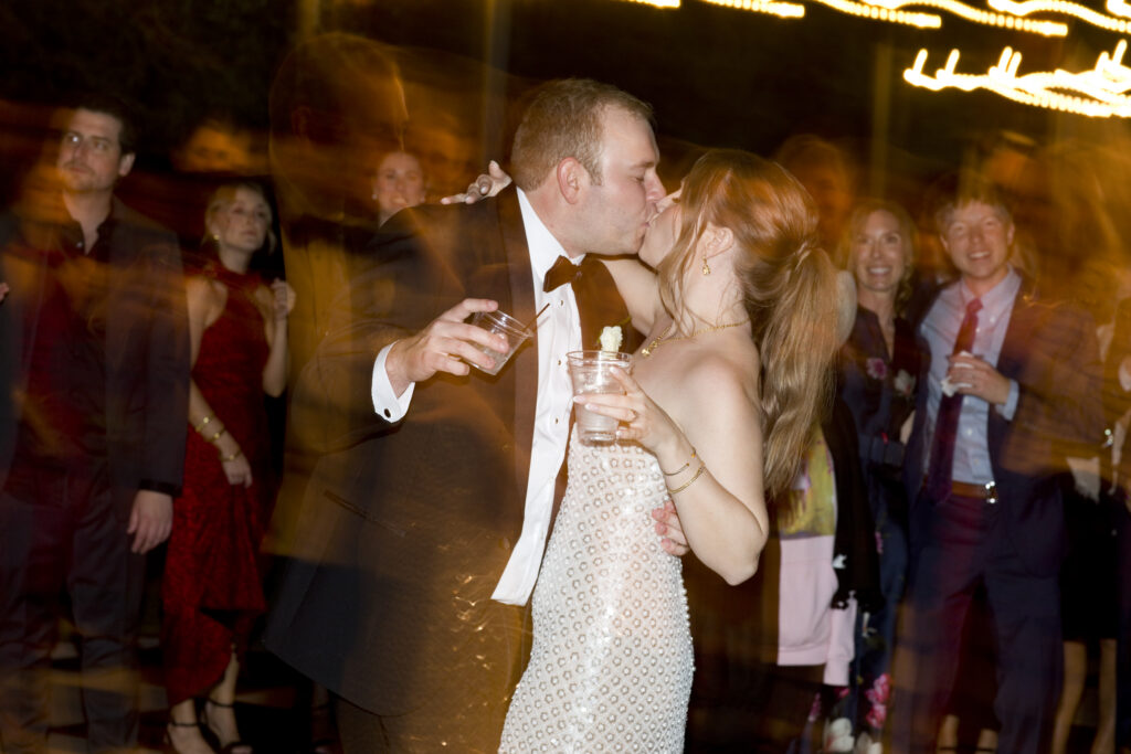 Bride and groom kissing during their wedding reception while guests celebrate